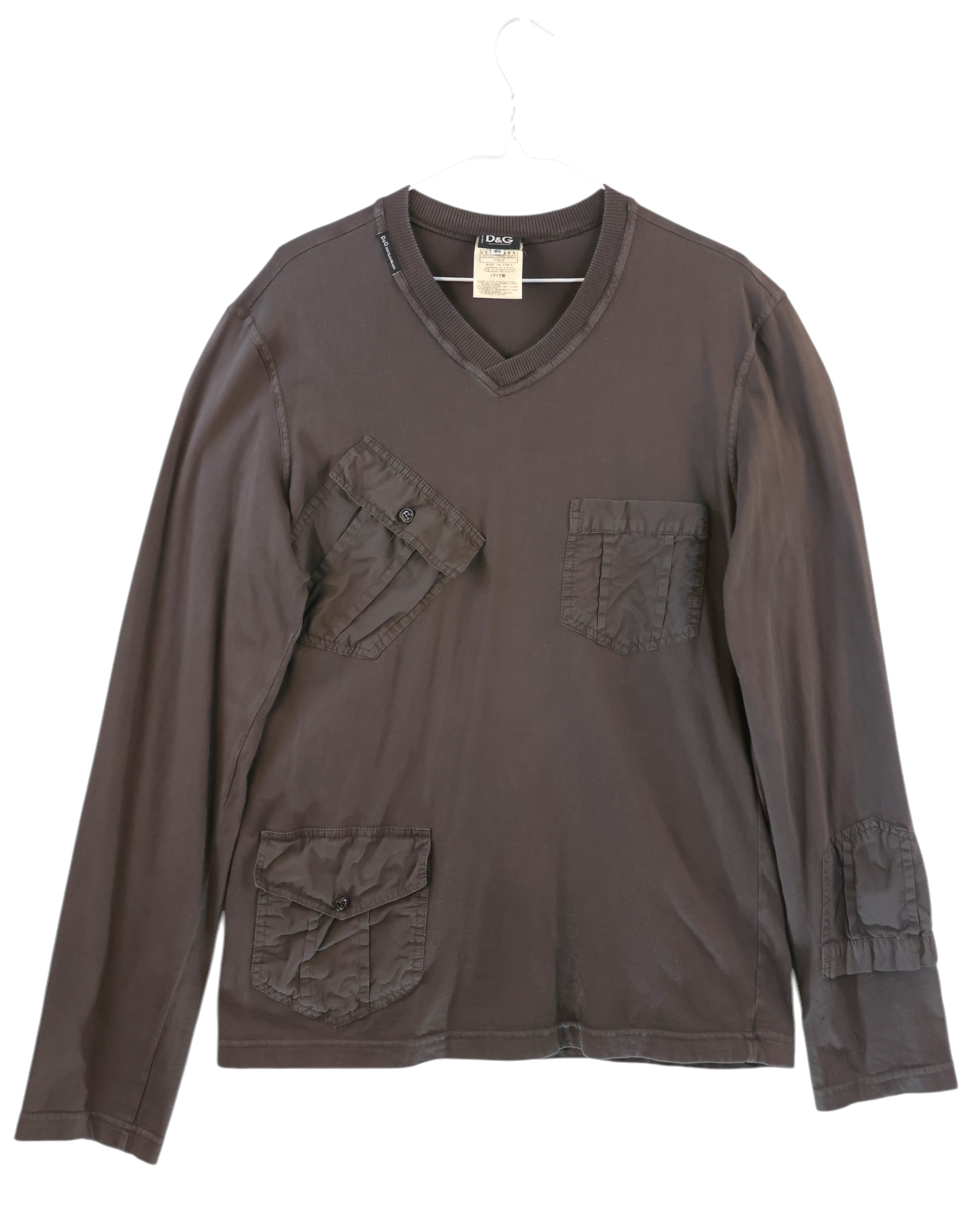 Brown long-sleeve shirt with pockets on a white background. Dolce & Gabbana brown/chocolate cotton long-sleeve T-shirt; V-neck, multiple flat/cargo patch pockets at chest, hip and sleeve with flap + button details, ribbed collar, tonal stitching; relaxed modern fit, unisex; great for denim, cargos, layering; utility/military/Y2K/minimal; Italian luxury house heritage.