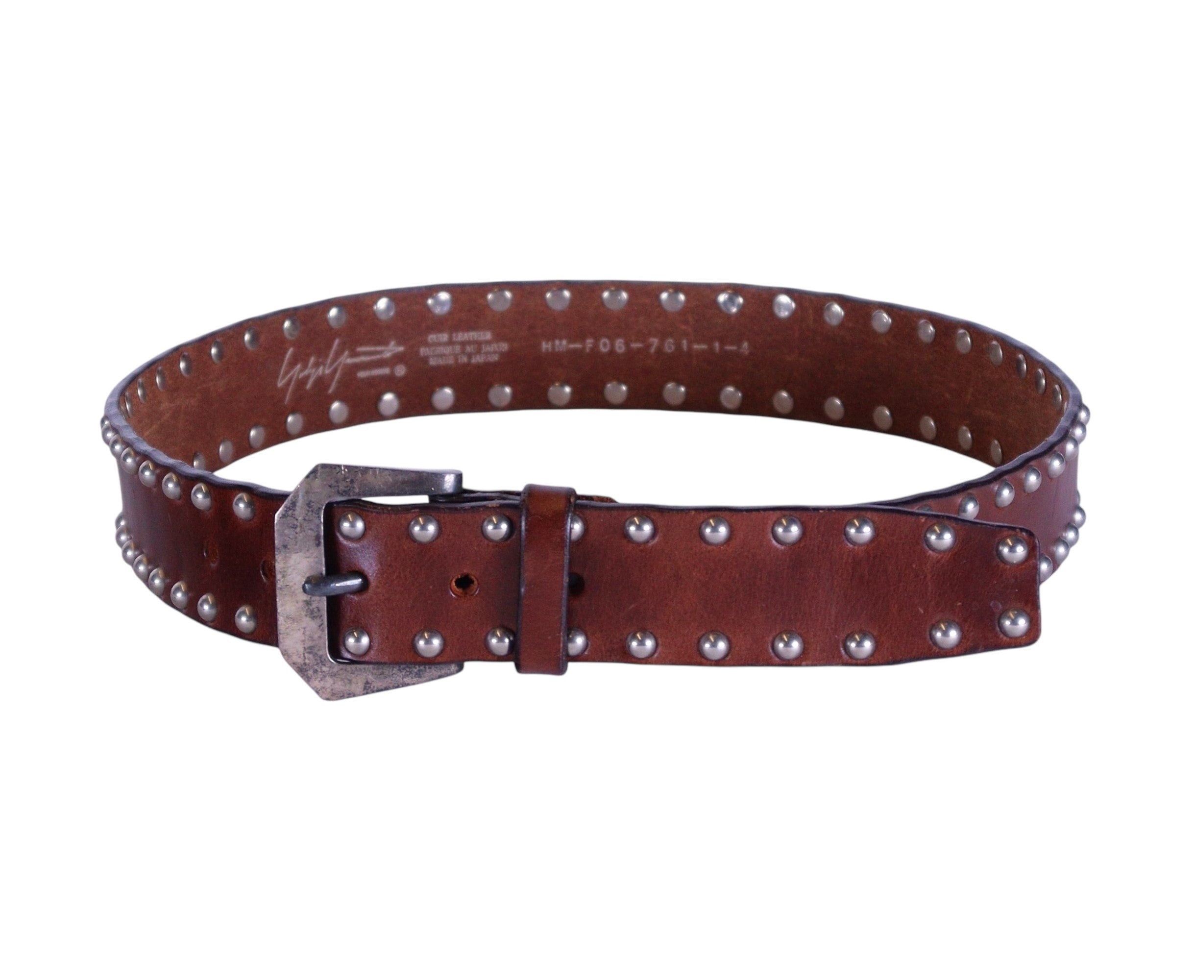 A brown leather belt with a studded rivet pattern and a metal buckle, presumably made by Yohji Yamamoto.Brown leather belt with all-over silver-tone studded rivets and a burnished square buckle, medium width; rocker/biker/cowboy vibes, unisex, gently worn, designer accessory. From Yohji Yamamoto—Japan’s avant-garde icon (Tokyo–Paris) celebrated for artisanal craft and deconstructed tailoring; luxury, rare, vintage belt.