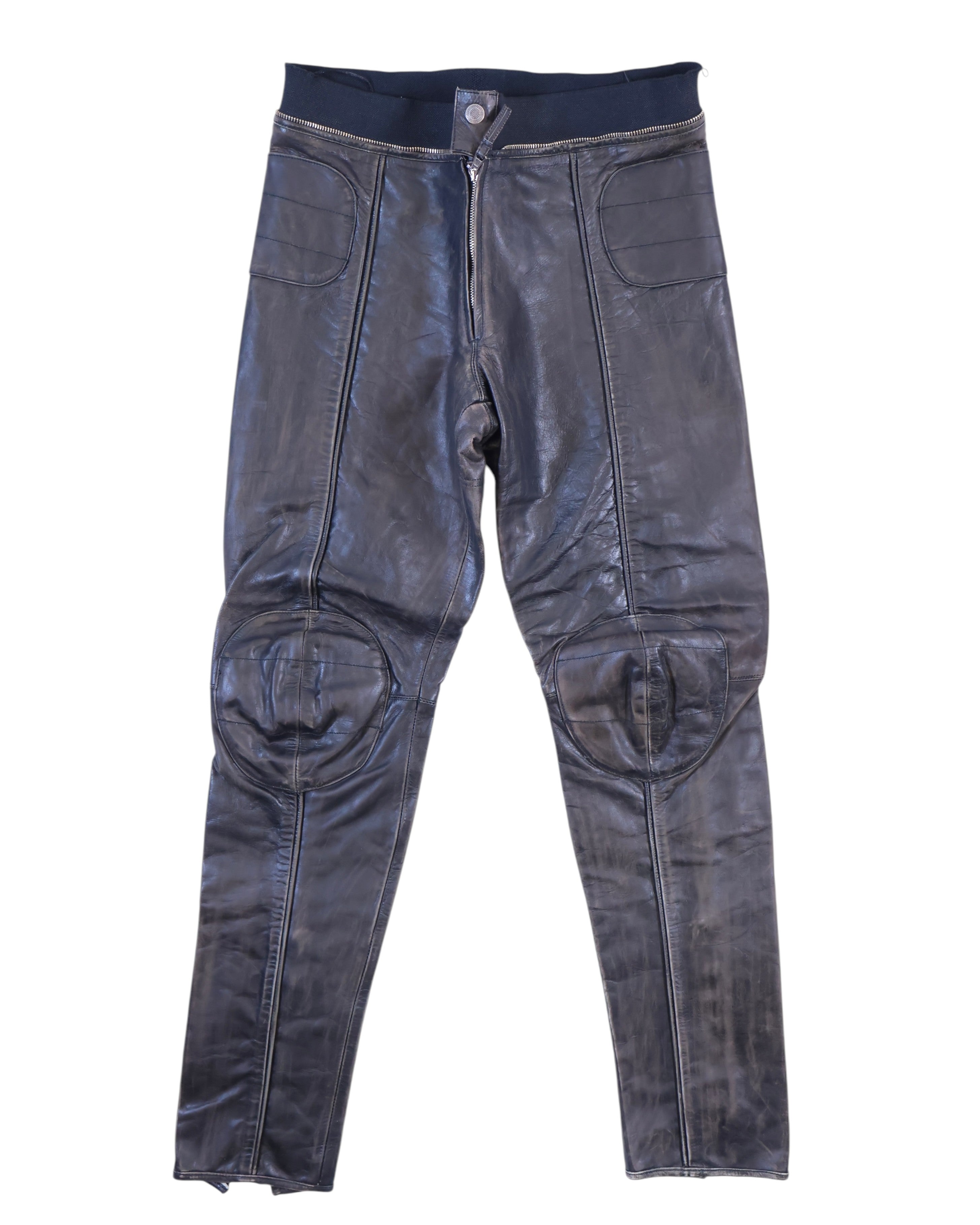 Vintage 1990s Jean Paul Gaultier black leather pants/trousers with moto biker detailing—padded rounded knees, paneled seams, front zip with snap and rib-knit waistband. Slim tapered leg; high-end, rare and unique piece laid flat on white.