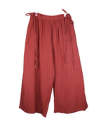 second hand Caravana autumn-red (rust/terracotta) bohemian pants/trousers in lightweight woven fabric, relaxed wide-leg palazzo/culotte cut with gathered waistband and adjustable side tie fastenings. Flowing, airy silhouette with clean hems; luxury artisan piece, rare and unique, laid flat on a white background.