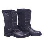 A pair of John Varvatos black leather boots with a buckled strap and metal studs on the side. John Varvatos black leather mid-calf boots with round toe, stacked heel and harness-style buckle strap, plus studded front panels and a top buckle. Grained finish with a rugged moto/engineer vibe; vintage, designer, rare.