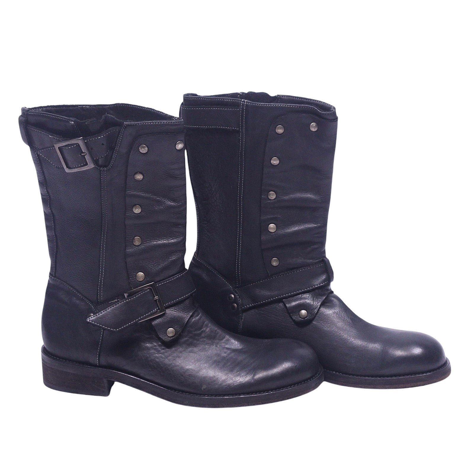 A pair of John Varvatos black leather boots with a buckled strap and metal studs on the side. John Varvatos black leather mid-calf boots with round toe, stacked heel and harness-style buckle strap, plus studded front panels and a top buckle. Grained finish with a rugged moto/engineer vibe; vintage, designer, rare.