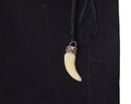 Close-up of a shark-tooth–style pendant charm with metal cap hanging from a leather cord at the waistband of black Voyage Mazzilli Michielsens jeans, showing tonal stitched/appliqué seam detail on twill denim.