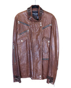 A brown Dolce & Gabbana sheepskin leather jacket with multiple zippers and a collar. Dolce & Gabbana brown/cognac sheepskin leather biker jacket; asymmetrical snap-over front, funnel collar with throat latch, multiple zip and snap-flap pockets, zip cuffs, buckle straps at hem; silver-tone hardware; regular fit, unisex; great with denim, tees, boots; moto, biker, rocker, Y2K; brand context: Italian luxury house, made in Italy, artisanal finish; vintage, lightly distressed texture.