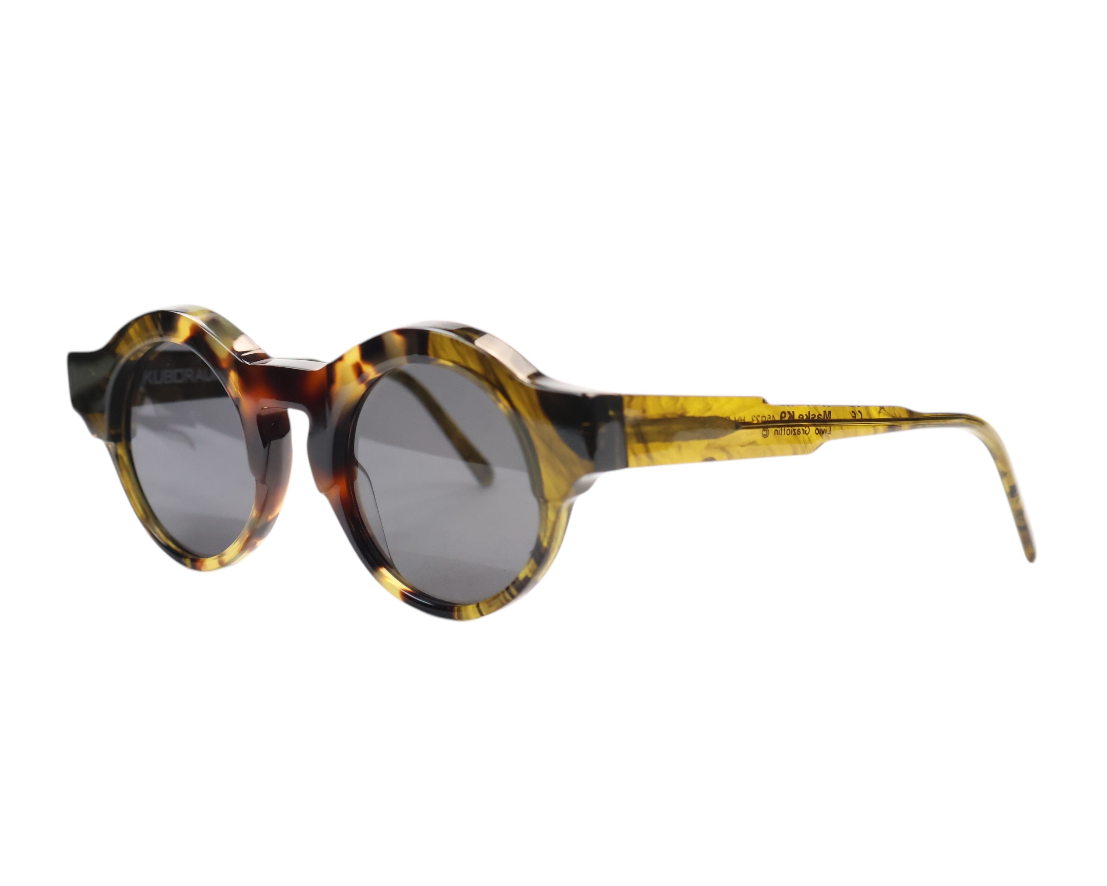 A pair of round full frame sunglasses with a patterned frame, likely to be displayed against a white background. Kuboraum Maske K9 tortoiseshell/amber-horn acetate round sunglasses; chunky sculptural beveled rims and wide temples with grey lenses; lightweight, comfortable, unisex; works with tailoring, streetwear, artwear, festivals; avant-garde/arthouse/Berlin design; brand born in Berlin, handmade in Italy, luxury indie eyewear, rare model.