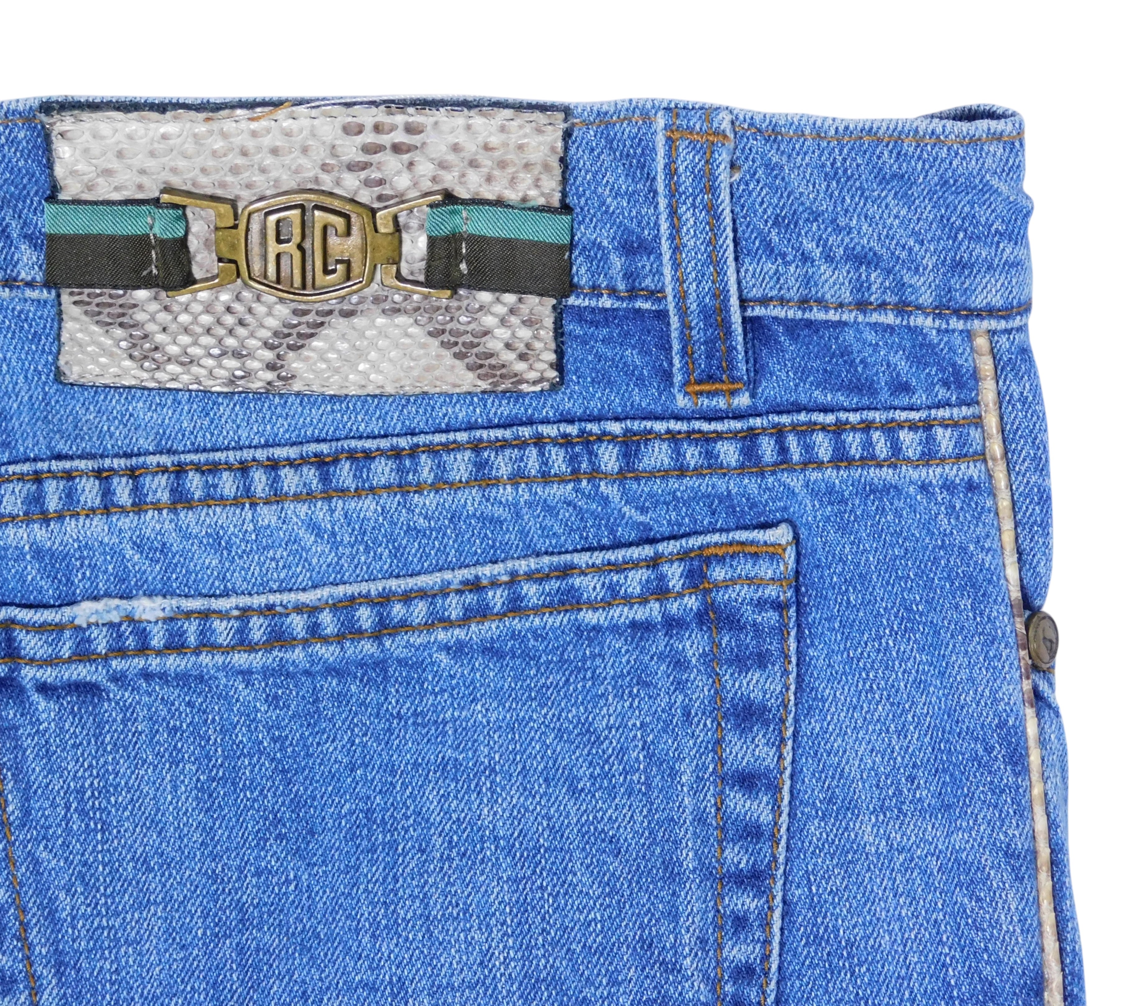 back waistband on vintage Roberto Cavalli blue jeans showing a snakeskin-pattern patch with RC monogram hardware and striped ribbon, plus contrast stitching; designer detail shot.