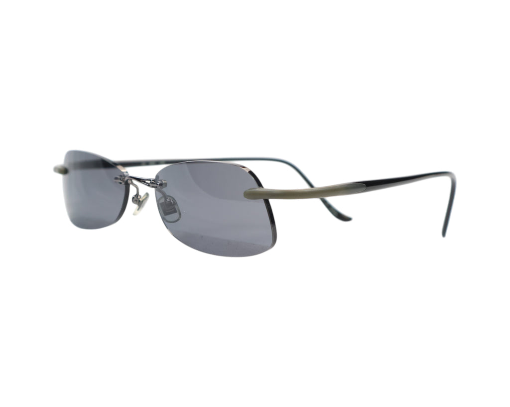 A pair of rimless sunglasses with dark lenses and metallic frame. Kata sunglasses / shades / eyewear — rimless drill-mount design with smoke-grey lenses, sleek metal/titanium bridge, ultra-thin wire temples with rubberized sleeves; lightweight, minimalist, unisex fit. Brand context: Kata is a design-led eyewear label rooted in Japanese minimalism and precision engineering, known for lightweight titanium pieces often crafted in Japan—collectible luxury sunglasses.