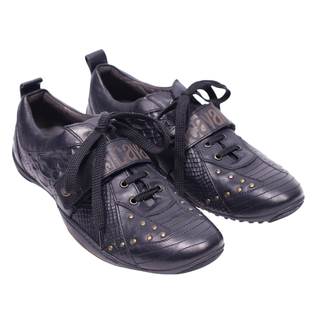 A pair of black Just Cavalli leather sneakers with snake-embossed patterns and studded details. Black low-top sneakers with snake-embossed panels, lace-up front and rounded toe, dotted with small gold studs and a logo strap across the tongue. Mixed-texture leather with a low rubber sole; vintage designer, rare.