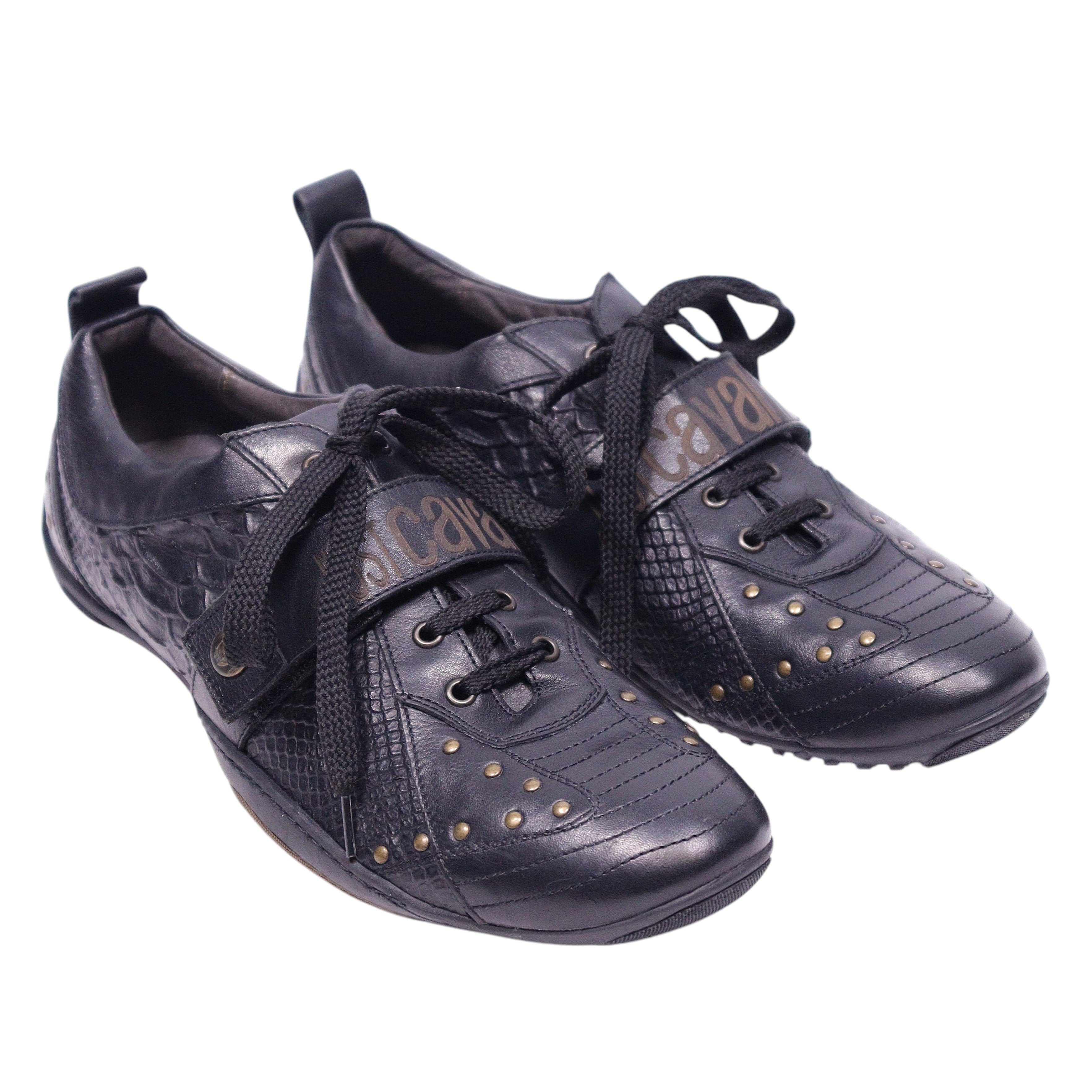 A pair of black Just Cavalli leather sneakers with snake-embossed patterns and studded details. Black low-top sneakers with snake-embossed panels, lace-up front and rounded toe, dotted with small gold studs and a logo strap across the tongue. Mixed-texture leather with a low rubber sole; vintage designer, rare.