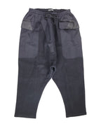 Second-hand vintage Damir Doma black sweatpants/joggers with drawstring waist and drop-crotch, tapered cropped legs, oversized front patch pockets with leather-trimmed flaps and mixed-fabric panels; minimalist avant-garde streetwear, rare designer piece laid flat on white.
