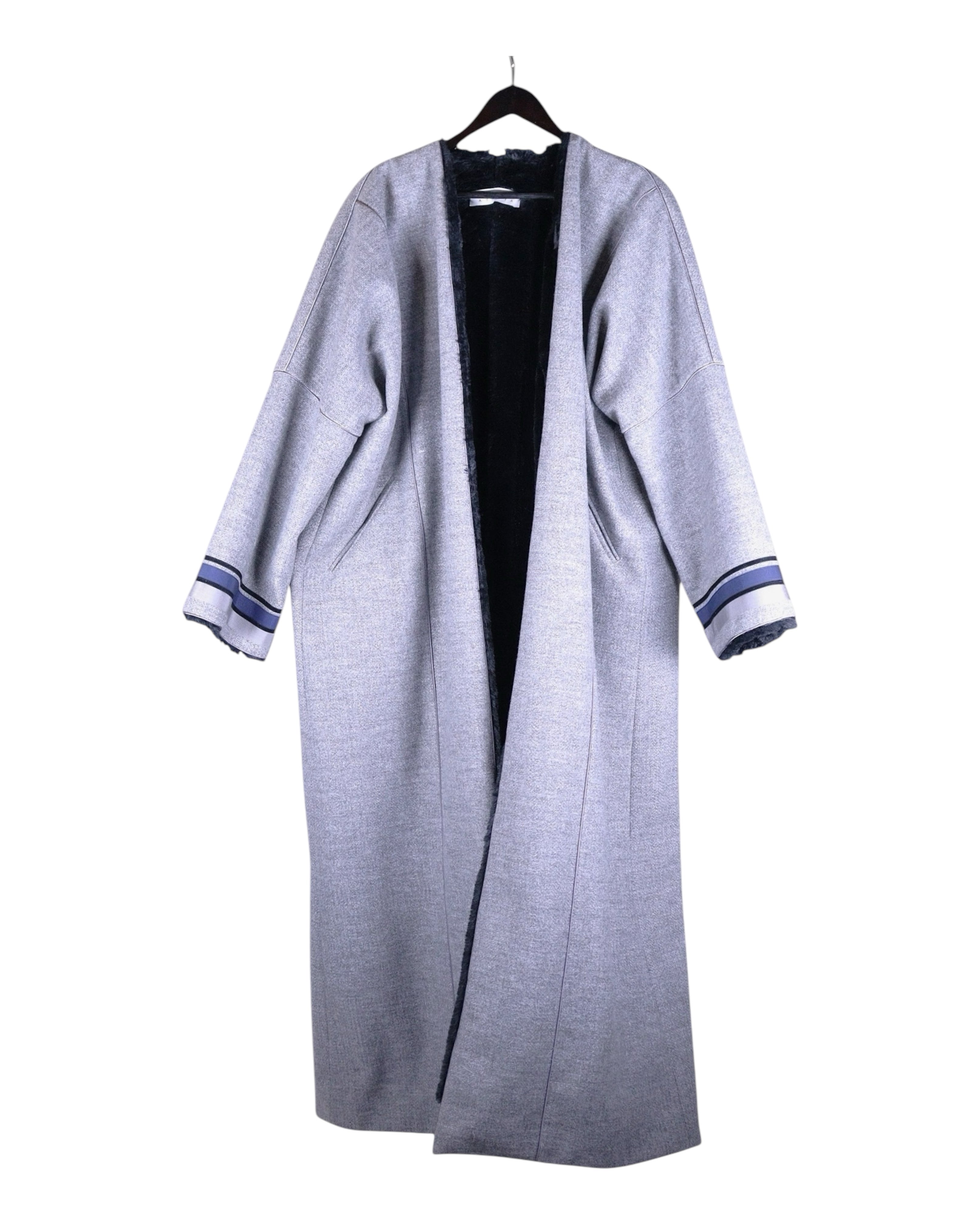 A long, gray faux fur lined jacket with blue accents on the cuffs, displayed on a hanger. Abadia grey farwa coat/jacket/overcoat/duster/robe; open-front maxi length, dropped shoulders, wide sleeves with striped cuffs; plush faux-fur lining for warmth; oversized relaxed fit, unisex-friendly; great over abayas, dresses, denim, for travel and winter layering; tags: modest, minimalist, bohemian, contemporary, heritage; Abadia (Saudi, artisan-led, Middle-Eastern craft roots), limited piece.