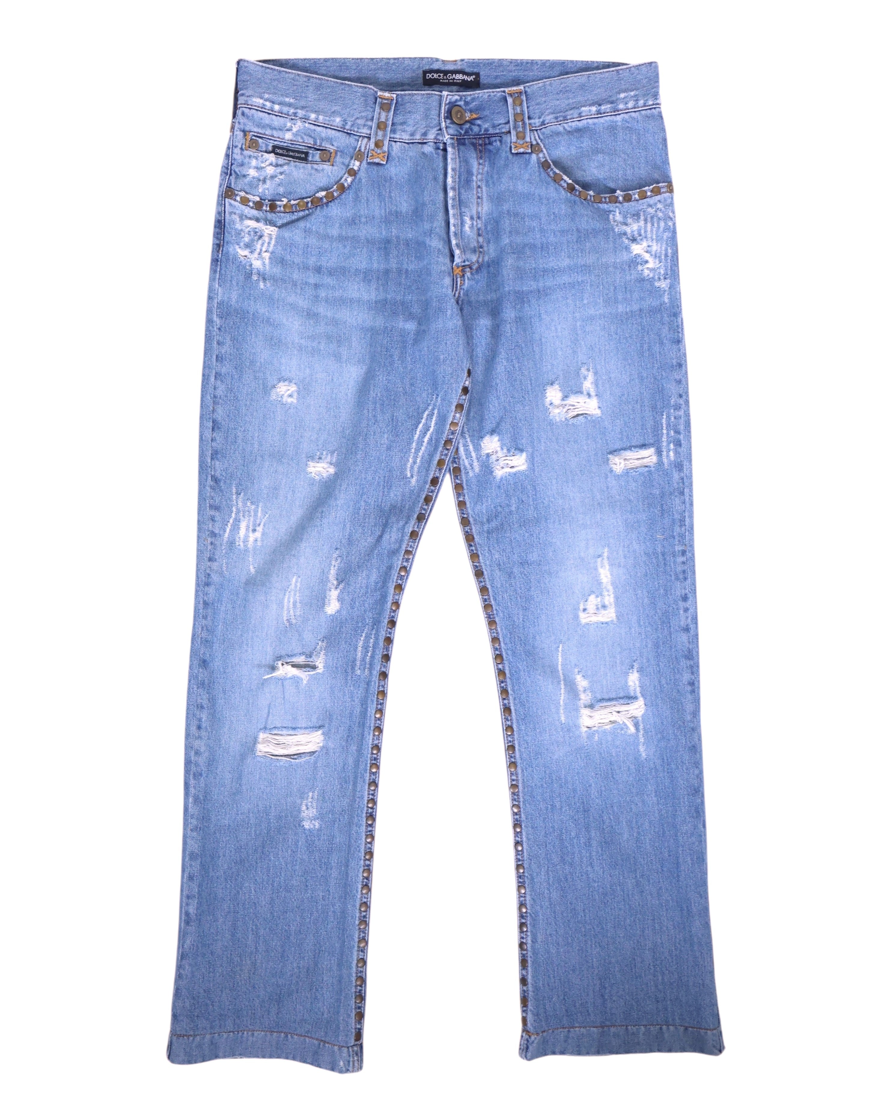Vintage Dolce & Gabbana light-wash jeans/denim trousers with studded-trim pockets and side seams, mid-rise straight leg and five-pocket, button-front styling, distressed with rips and whiskering. Luxury designer, rare piece laid flat on white.