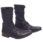 A pair of dark brown leather boots with a lace-up front and a low heel on a plain background. Christian Peau dark brown leather lace-up boots with a mid-calf shaft, round cap toe and low stacked heel. Grained leather with vintage, rugged patina; artisanal, designer, rare.