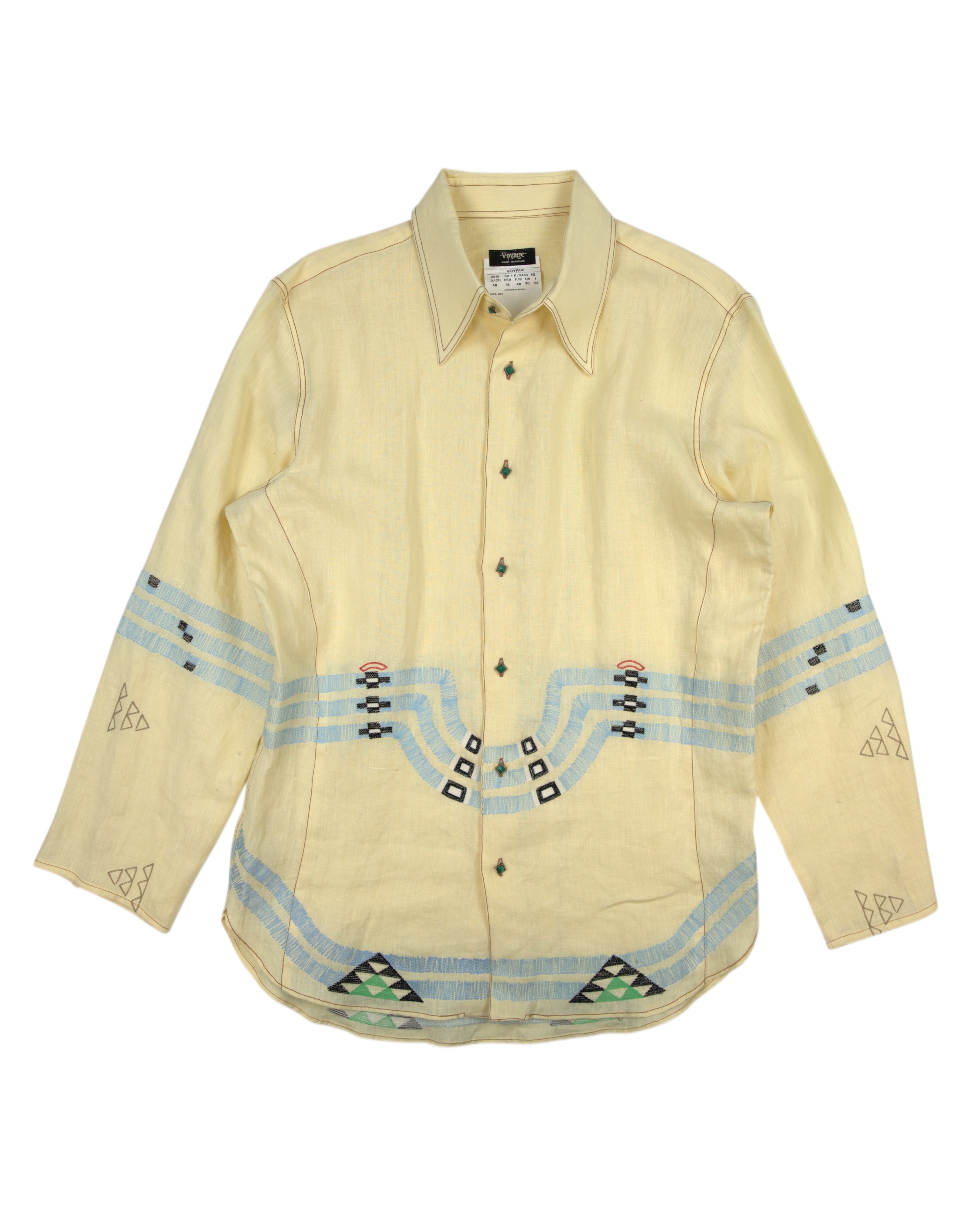 Beige shirt with decorative patterns on a white background. Vintage Voyage by Mazzilli & Michielsens embroidered dress shirt / button-down / collared top in pale butter yellow; geometric folk/tribal-inspired needlework in sky-blue, sage green and black across chest, sleeves and hem; long sleeves, pointed collar, curved hem, lightweight woven fabric for a relaxed tailored fit; artisan craftsmanship from Belgian designer duo (1990s–Y2K era); boho, artsy, gallery, festival, unisex styling—European luxury with 