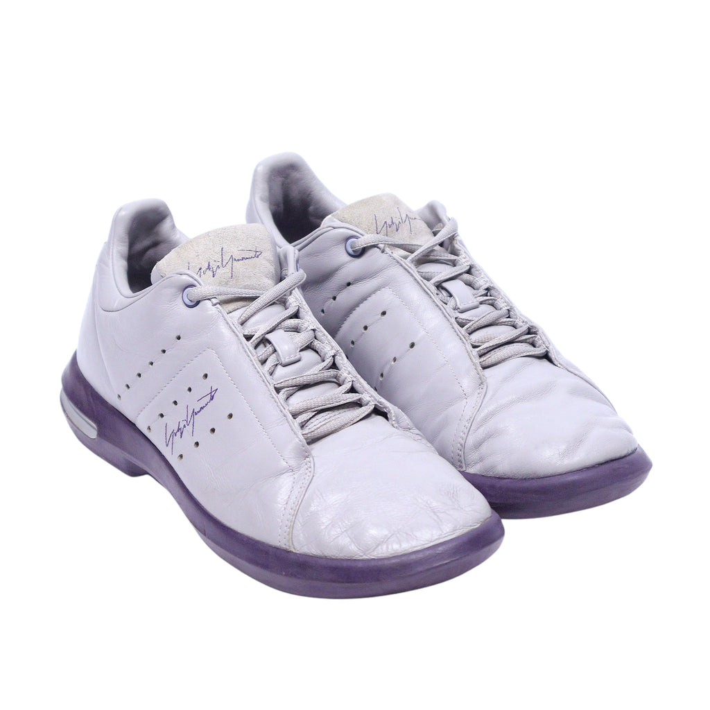 A pair of Yohji Yamamoto adidas sneakers with gray and purple color scheme. Yohji Yamamoto x adidas 2002 gray leather sneakers with purple sole, perforations, lace-up front, and signature detail.