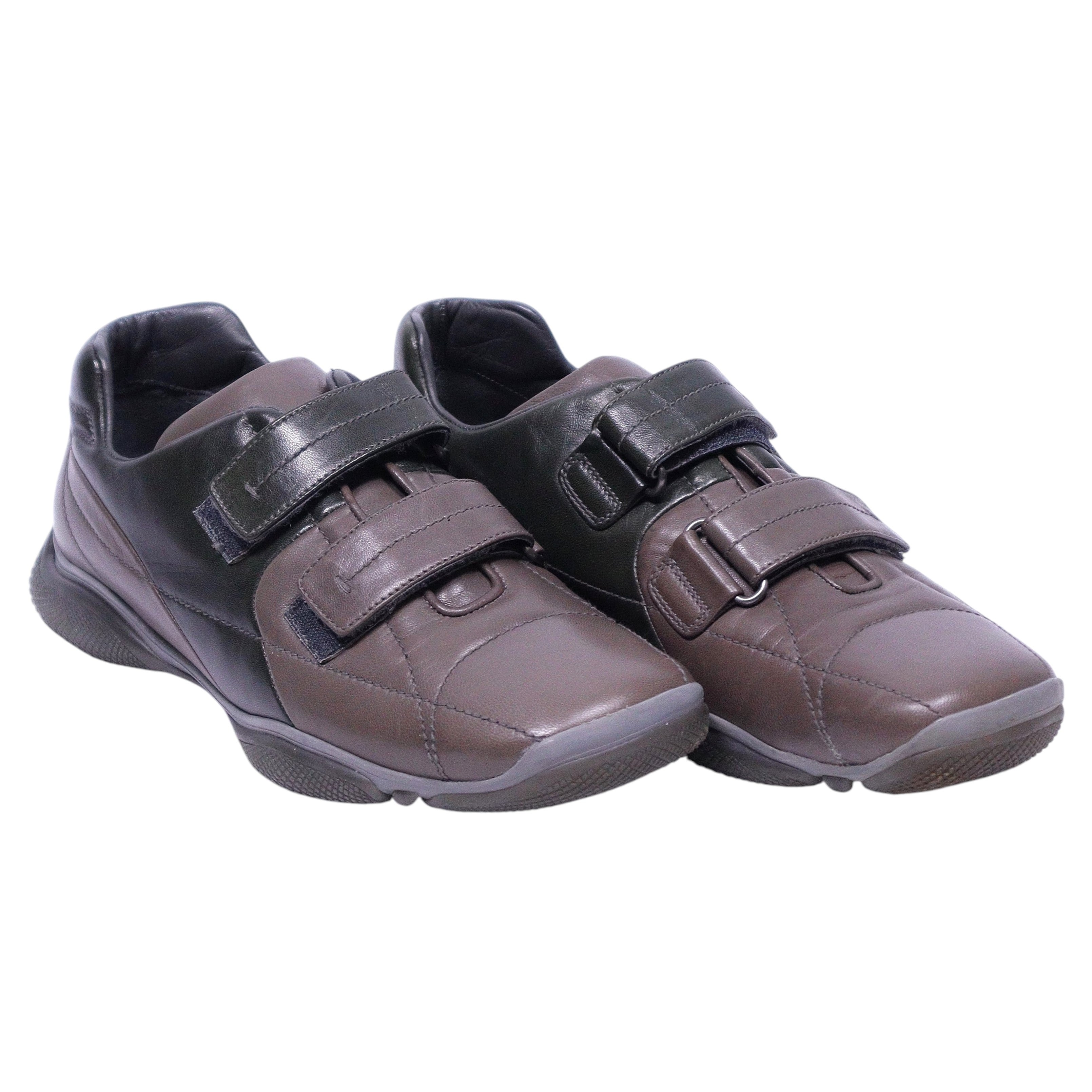 A pair of Prada brown and black leather sneakers with hook and loop closures. Prada brown and black leather low-top sneakers/trainers with double hook-and-loop straps, round toe and cushioned rubber sole. Sleek mixed-panel design; vintage luxury, rare.
