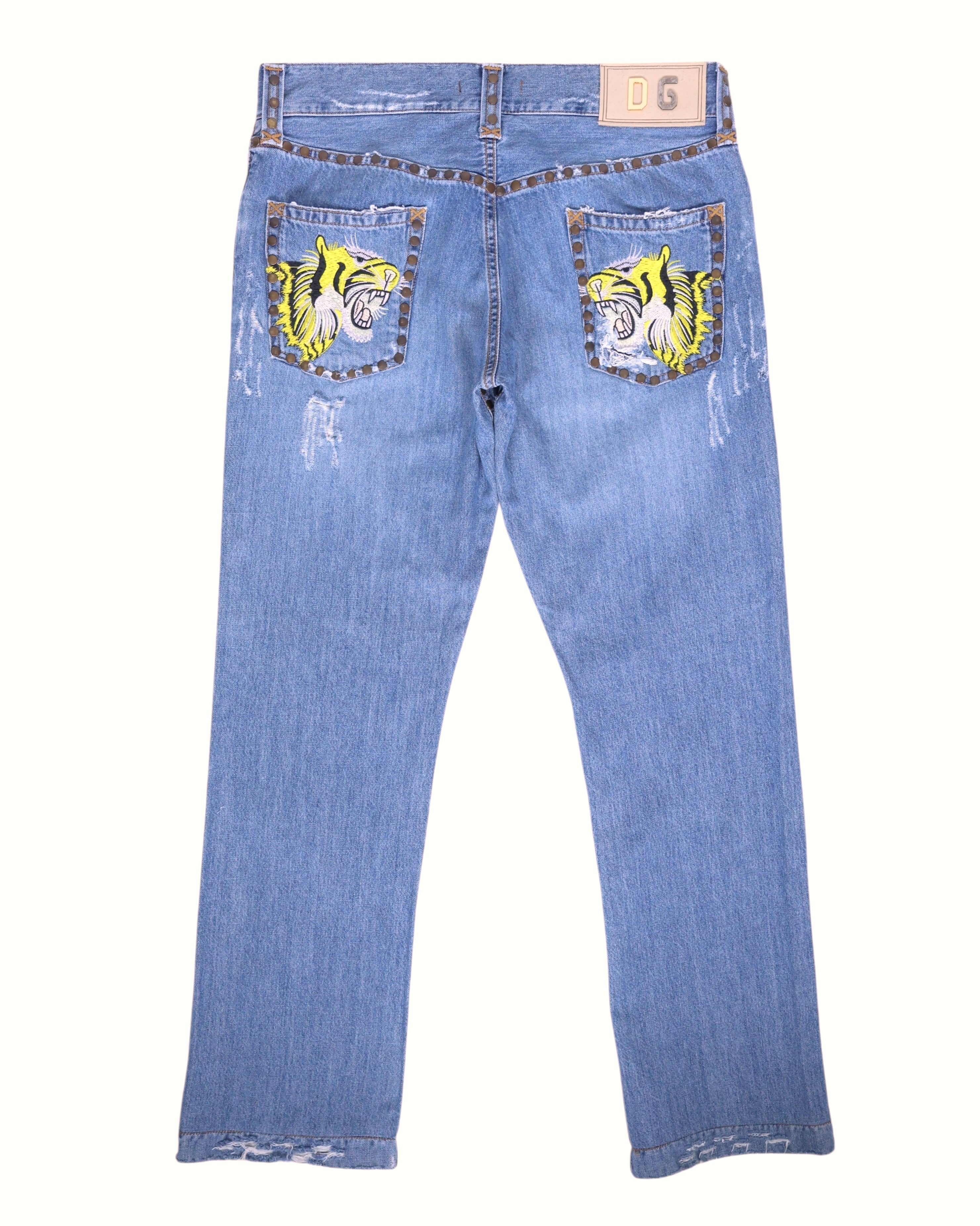Vintage Dolce & Gabbana light-wash jeans, back view, featuring twin roaring tiger embroidery on the back pockets, studded trims, contrast stitching and light fraying at the hems; straight-leg cut. Luxury designer, rare and unique, laid flat on white.