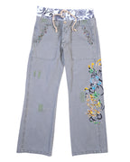 RA-RE washed grey trousers with relaxed straight legs, large front patch pockets with studded trim, visible repair patches, and a bold multicolour scroll embroidery down the right leg. A contrast printed waistband with rope drawcord peeks out; boho-meets-streetwear, designer, second-hand and unique.