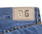 Close-up of vintage Dolce & Gabbana light-wash blue denim jeans/denim trousers showing a beige DG logo patch with mixed-metal letters, studded rivet trim and contrast stitching. High-end designer detail shot—rare, unique, luxury denim.