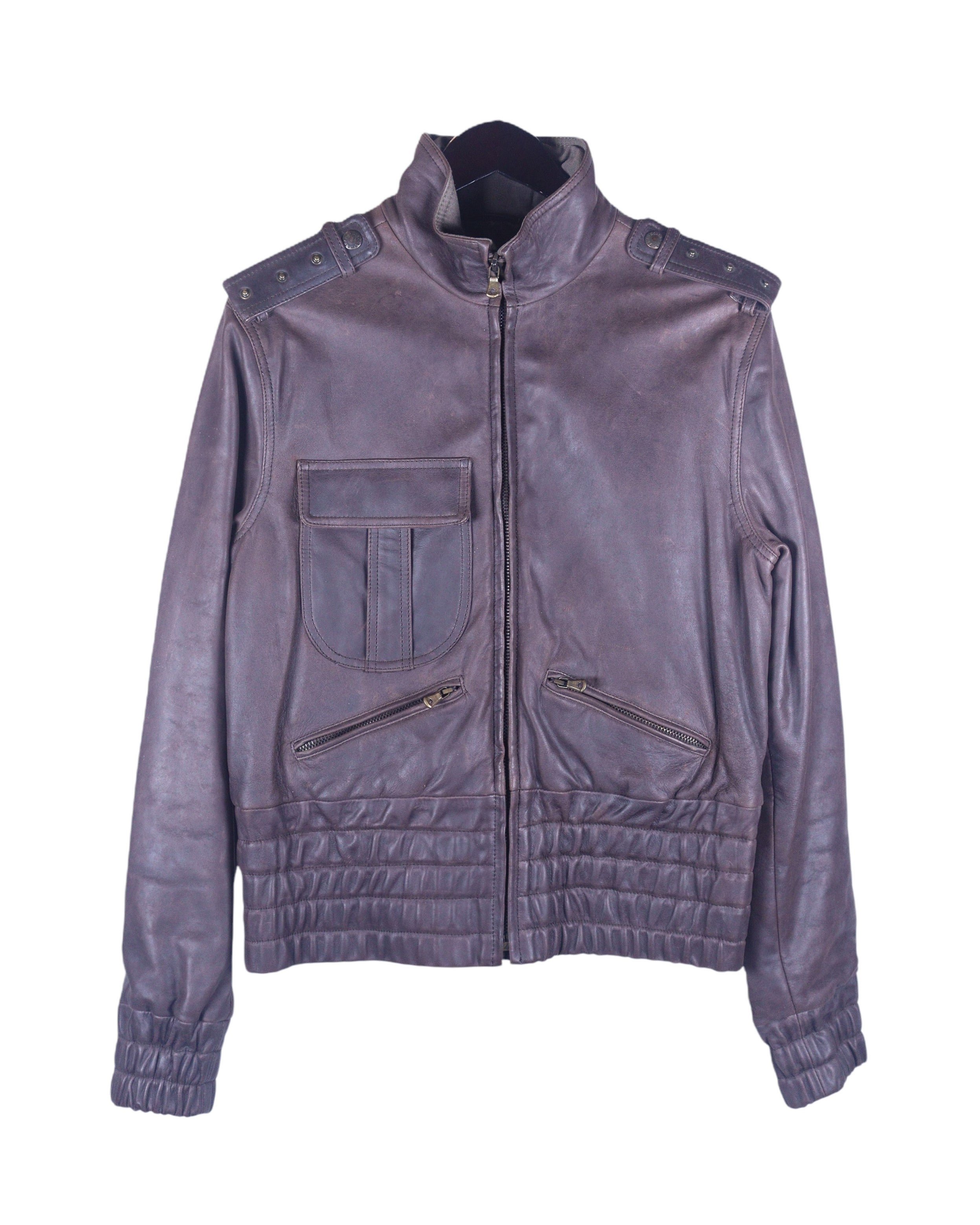 A brown Dolce & Gabbana goatskin leather jacket with a mandarin collar, zipper details, and a quilted design on the lower section. Dolce & Gabbana dark plum/brown goatskin leather jacket; stand collar, studded epaulettes, zip front, flap chest pocket with twin slanted zip pockets, quilted/smocked hem and cuffs; antique-brass hardware; regular fit, unisex; great with denim, tees, boots; style: moto, military, rocker, Y2K; brand context: Italian luxury house, made in Italy.