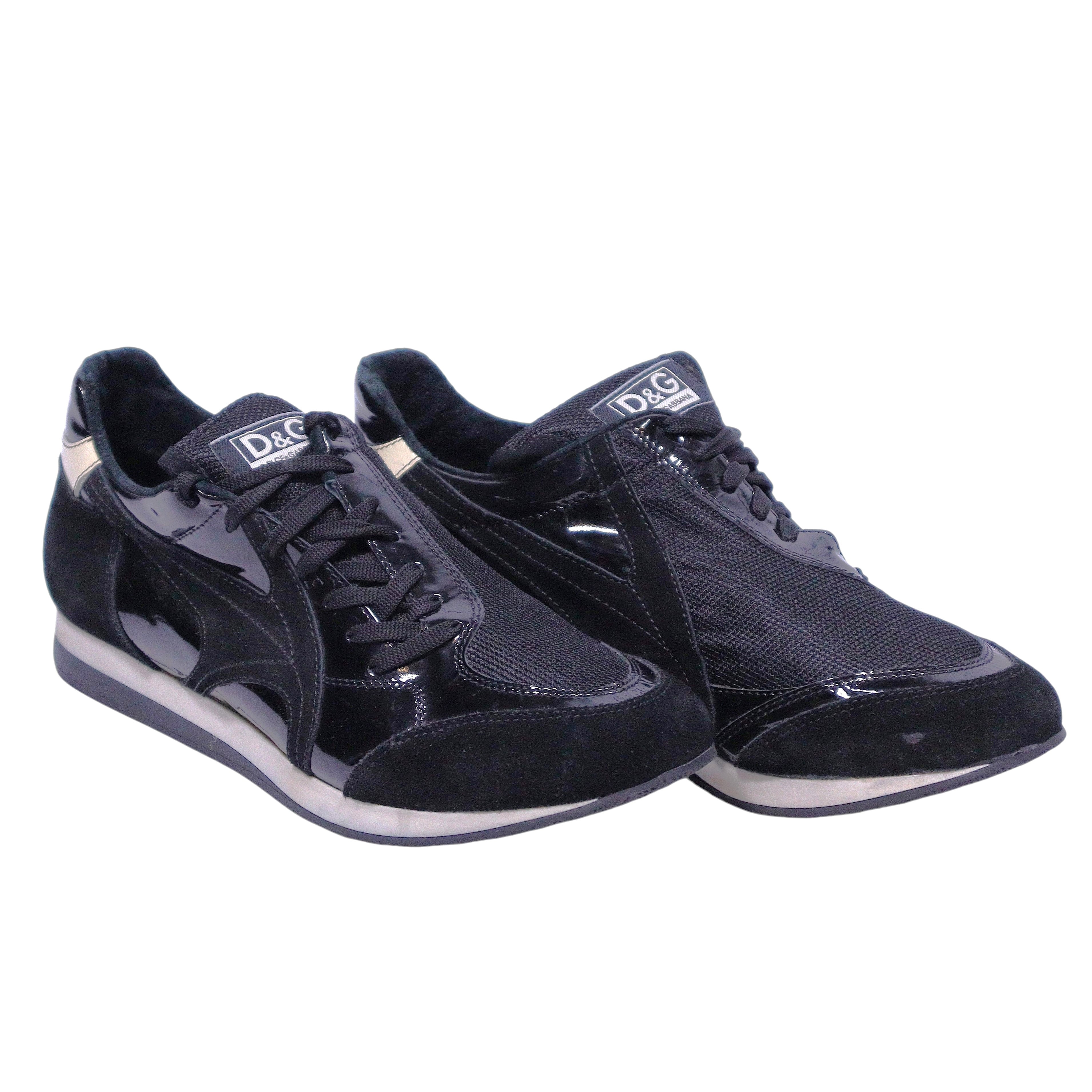 A pair of Dolce Gabbana leather suede sneakers in black color. Vintage D&G Dolce & Gabbana black low-top sneakers/trainers with mixed materials—smooth leather, suede and glossy patent overlays—mesh panels, lace-up front, logo tongue, gold heel tab, retro runner silhouette and cushioned white/black sole.
