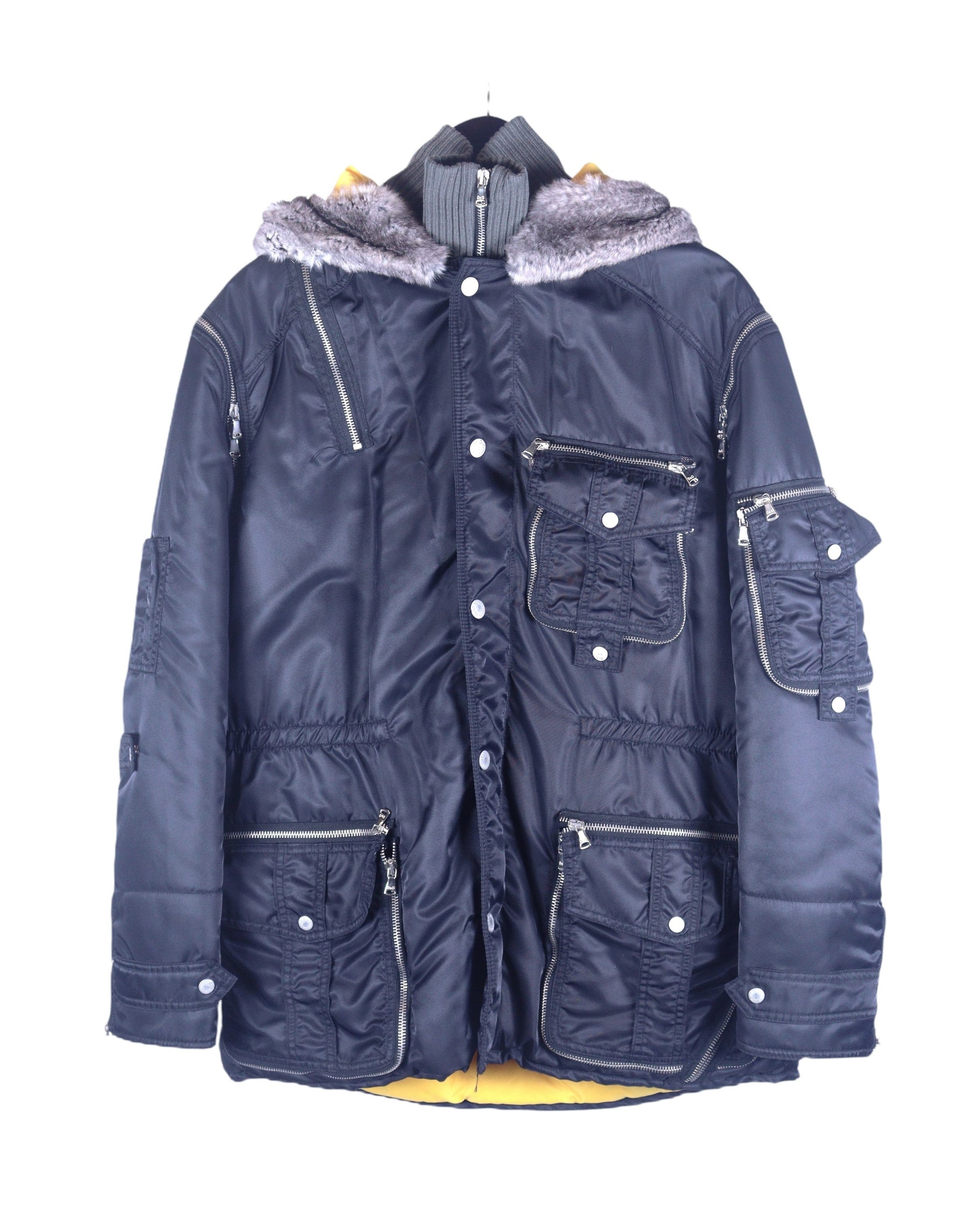A Dolce & Gabbana black coat with rabbit fur on the hood, multiple pockets, and a zipper closure. Dolce & Gabbana navy/black nylon parka coat with rabbit-fur hood trim; insulated shell, rib-knit stand collar insert, multi cargo pockets, zip/snap front, silver-tone hardware, contrast yellow lining; regular fit, unisex; winter, streetwear, denim; style tags: utility, military, Y2K; brand context: Italian luxury house, Made in Italy craft.