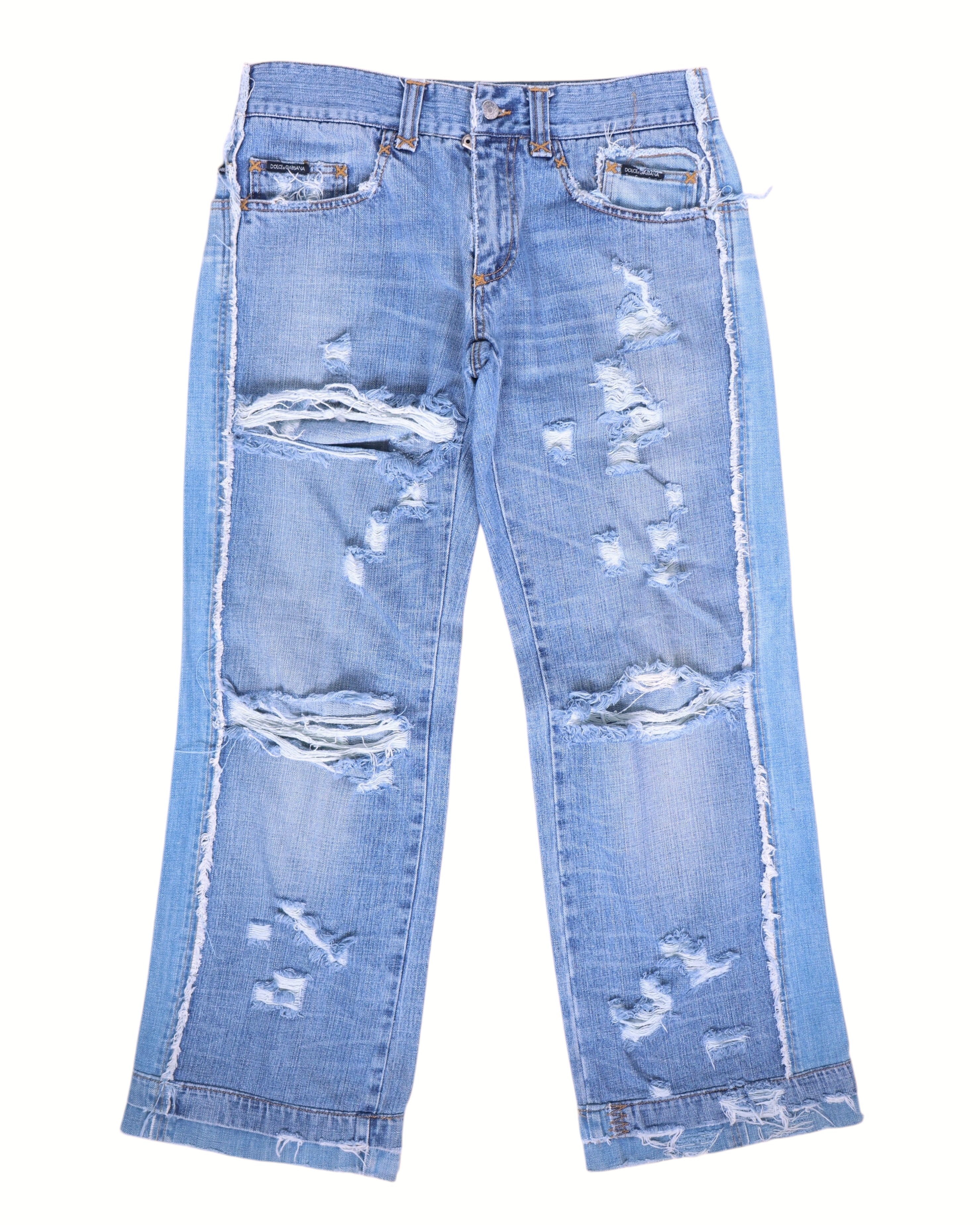Vintage Dolce & Gabbana Silver Label light-blue jeans/denim trousers with heavy distressed, ripped and shredded details, whiskering and fading; straight-leg, mid-rise five-pocket design with belt loops, button front, contrast side panels and raw frayed hems. High-end, rare designer pair laid flat on white.