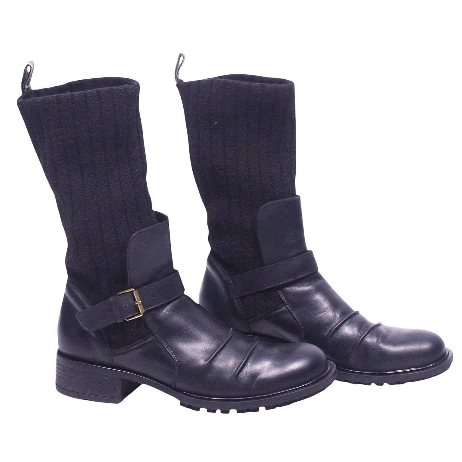 A pair of black leather boots with ribbed knit cuffs and buckle details, set against a white background. Roberto Cavalli black leather biker boots with ribbed knit shafts, buckle straps, round toes, and lug soles.