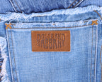 Detail shot of vintage Dolce & Gabbana light-wash denim back pocket with an embossed tan leather logo patch and raw, frayed waistband stitching. High-end designer jeans/denim, worn-in and rare.