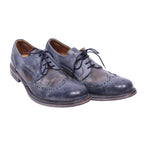 A pair of John Varvatos wingtip brogue shoes with laces, isolated on a white background. John Varvatos dark navy leather wingtip brogue derby shoes with open lacing, round toe and stacked sole. Lightly distressed finish with vintage patina; designer, rare.