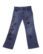 A pair of blue jeans with floral embroidery. Vintage Roberto Cavalli blue jeans/denim trousers with tonal floral embroidery/appliqué blooms on both legs, mid-rise straight-leg cut, five-pocket button waist, and gentle fading/whiskering, laid flat on white. Luxury designer piece—rare and unique. Blue straight-leg denim with tonal blooms and gentle fading