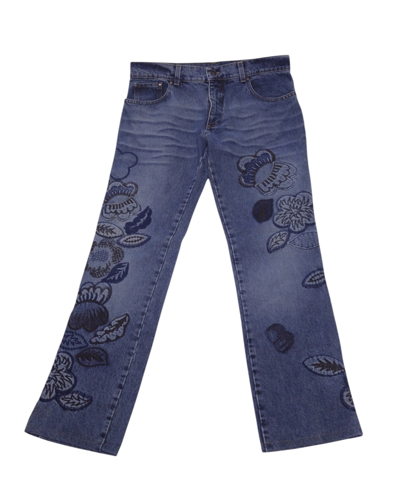 A pair of blue jeans with floral embroidery. Vintage Roberto Cavalli blue jeans/denim trousers with tonal floral embroidery/appliqué blooms on both legs, mid-rise straight-leg cut, five-pocket button waist, and gentle fading/whiskering, laid flat on white. Luxury designer piece—rare and unique. Blue straight-leg denim with tonal blooms and gentle fading