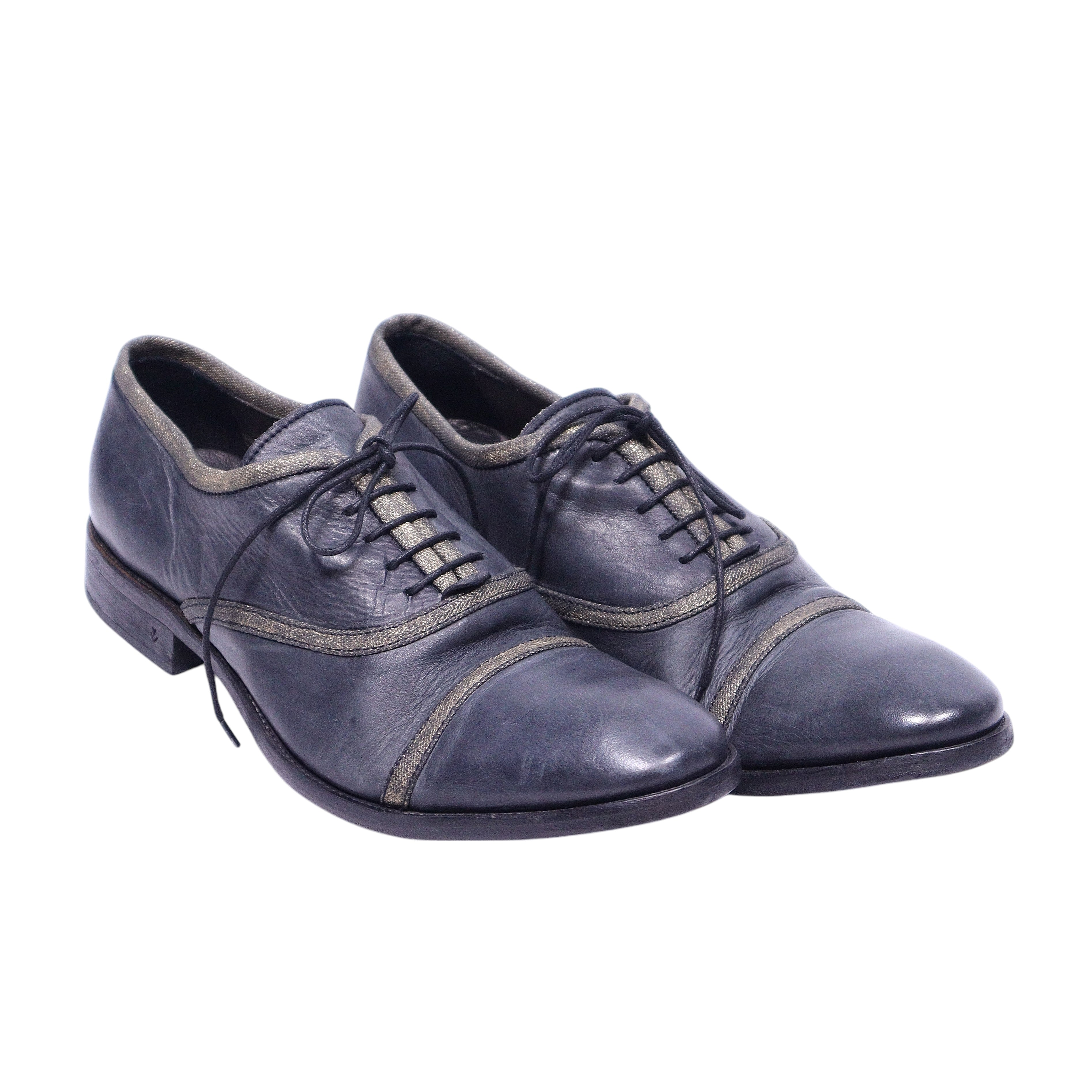 A pair of John Varvatos Richards bound collection leather oxford shoes, featuring a dark color with contrasting stitching and metal eyelets, placed against a white background.John Varvatos Richards Bound Collection cap-toe Oxfords in slate grey leather with closed lacing, metallic bound piping and a low stacked heel. Lightly distressed, vintage luxury and rare.