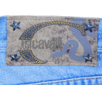 Back waistband label reading “Just Cavalli” on a suede patch decorated with star studs and a snake motif. Branding detail on worn blue denim; vintage, luxury, collectible.